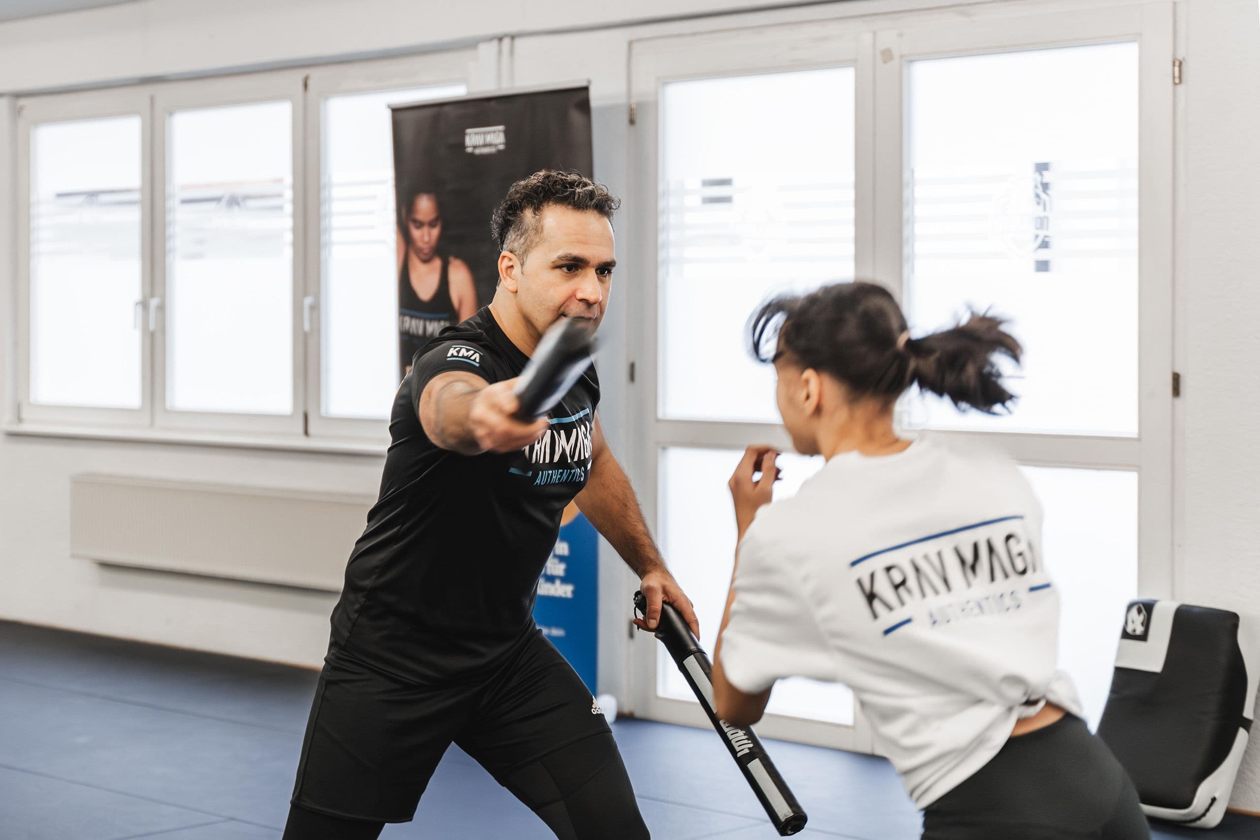 Krav Maga Training: Selbstverteidigung gegen Stockangriff mit Trainer und Teilnehmerin in Übungssituation